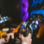 Close-up of hands gripping joysticks in a neon-lit arcade setting, capturing the gaming atmosphere.