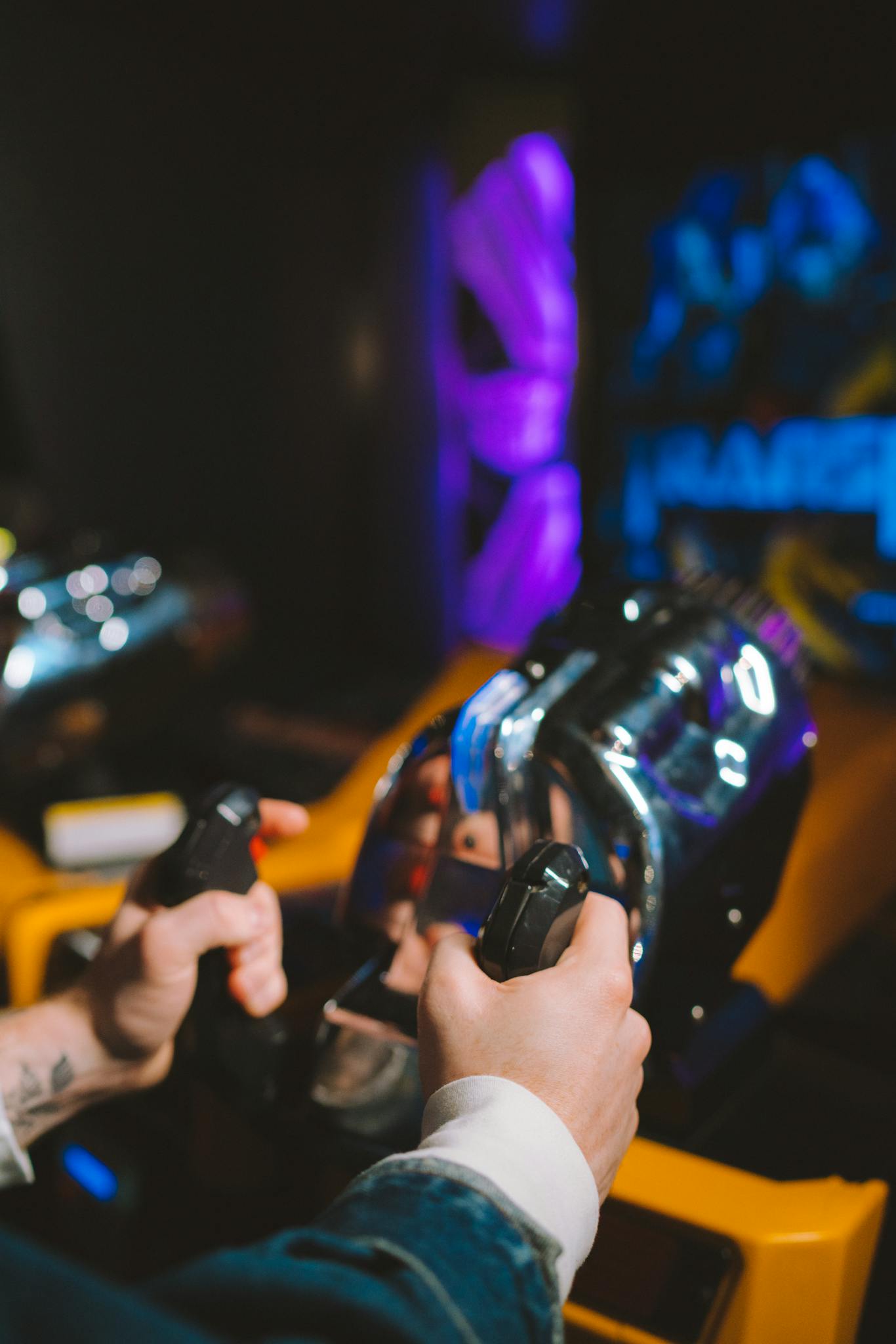 Close-up of hands gripping joysticks in a neon-lit arcade setting, capturing the gaming atmosphere.