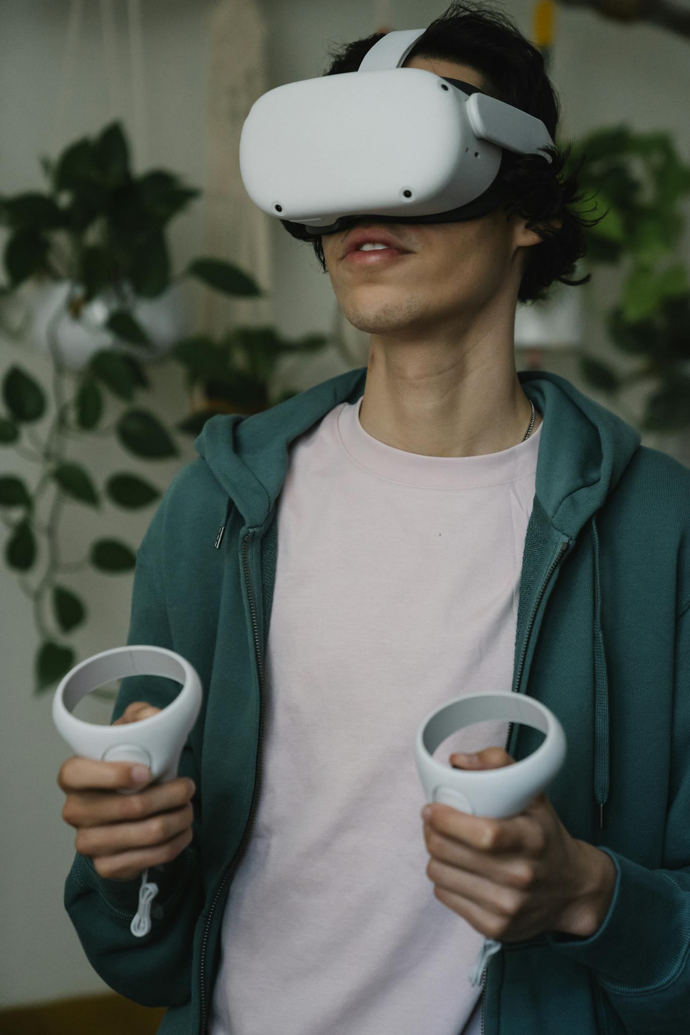 Male in virtual reality goggles with controllers playing video game while having free time in house