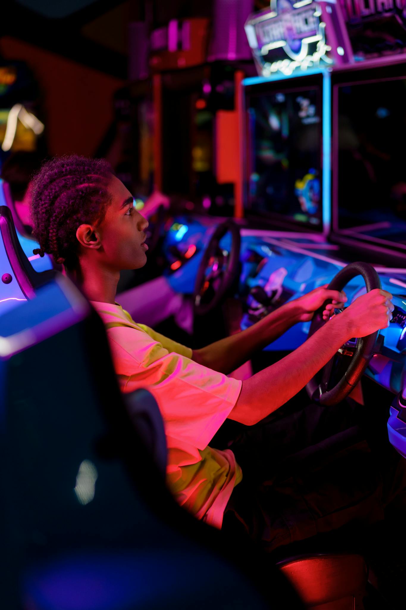 Young man playing a racing game at an arcade, immersed in vibrant neon lights.
